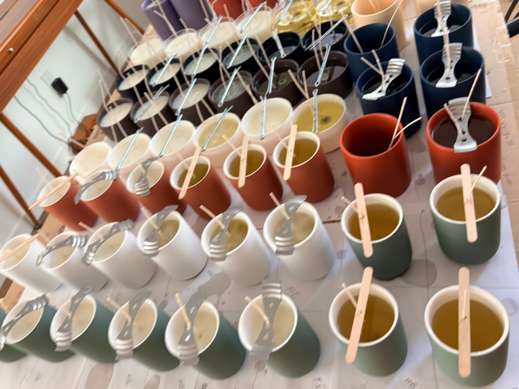 A whole line of colored vessels just poured, wicks held while the wax is still gold